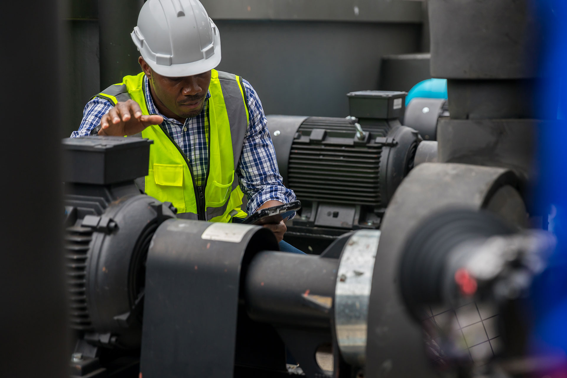 Industrial engineer in safety vest and hard hat inspecting large machinery with tablet